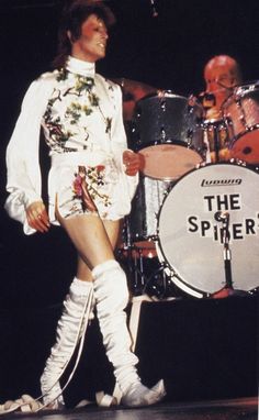 a man in short shorts and knee high boots standing on stage next to a drum