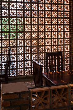 a wooden table sitting next to a window covered in latticed wood panels on top of a brick wall