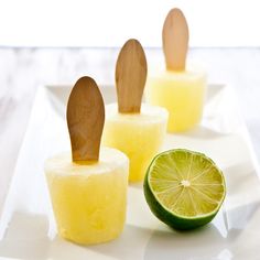 three popsicles with wooden spoons and lime slices on a white plate next to each other