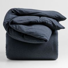 an unmade bed with dark blue sheets and pillows on top of each other, in front of a white background