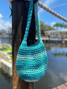 a blue crocheted bag hanging from a wooden post next to water and dock