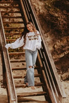 a woman standing on top of a set of stairs wearing jeans and a white shirt