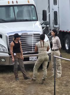 three women are standing in front of a semi - truck and one is talking to another woman