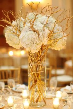 a vase filled with white flowers sitting on top of a table covered in plates and candles