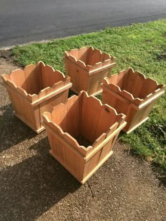 four wooden planters sitting on the ground in front of some grass and a road