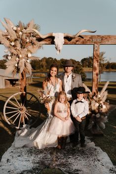 a bride and groom with their children in front of an old west styled wedding arch