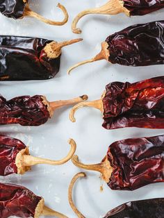 several red peppers are lined up on a white surface with wooden spoons next to them