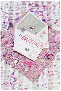 a pink and white wedding card with confetti on it, surrounded by flowers