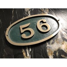 a green and gold house number sign on a black marble surface with the number 55