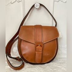 Padova Saddle Bag Classic Equestrian Style Is Easily Within Reach. This Crossbody Saddle Bag Perfectly Nods To Chic Sophistication No Matter The Occasion. You're Sure To Reach For It Time And Time Again Size/Profile: Petite Saddle Bag Walls: Full-Grain Leather Trim/Embellishments: Heavy, Hand-Crafted Stitching Handles/Strap: Adjustable, Flat Leather Crossbody Strap Exterior: Rear Slip Pocket Hardware: Metal Studs Closure: Flap Top With Magnetic Snap Closure And Buckle Lining/Trim: Faux Suede/Vel Saddle Bag Purse, Crossbody Saddle Bag, Leather Saddle Bags, Equestrian Style, Saddle Bag, Leather Care, Crossbody Strap, Leather Trim, Full Grain Leather