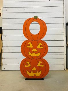 three pumpkins sitting on top of each other in front of a white wall with wood planks