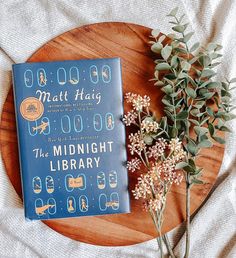 a book sitting on top of a wooden table next to some flowers and greenery