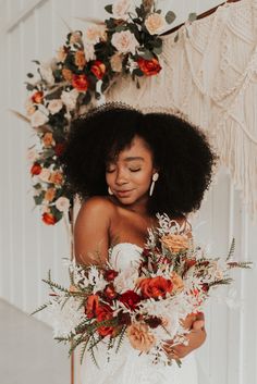 a woman with an afro holding a bouquet of flowers and greenery in her hands