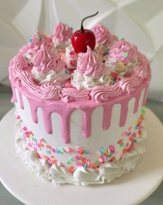 a white and pink cake with sprinkles and a cherry on the top