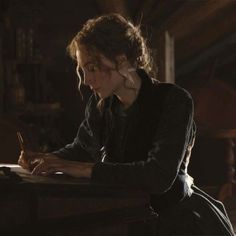 a woman sitting at a desk writing on a piece of paper with a pen in her hand