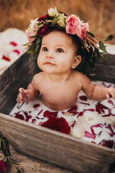 a baby wearing a flower crown sitting in a wooden box with flowers on it's head