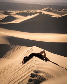 a woman laying on top of a sand dune in the middle of the desert at sunset