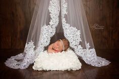 a baby wrapped in a wedding veil is laying on a white fluffy pillow under the bed