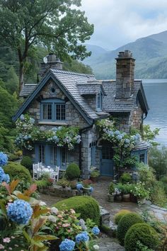 a stone house with blue shutters and flowers around it