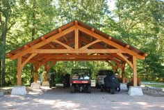 two vehicles parked under a wooden structure in the middle of a park with lots of trees