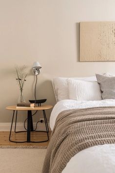 a bed with white sheets and pillows in a bedroom next to a lamp on a table