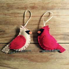 two felt bird ornaments are hanging on a wooden surface, one is red and the other is white