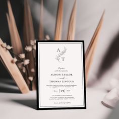 an elegant wedding card with the letter t on it sits next to some flowers and reeds