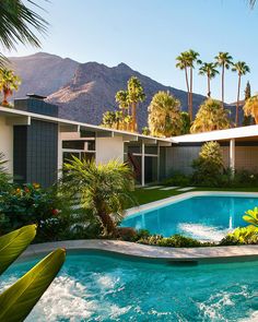 a swimming pool surrounded by palm trees in front of a house with mountains in the background