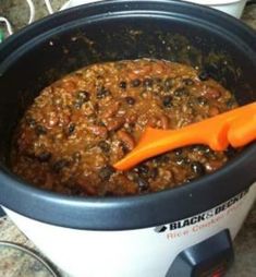 a crock pot filled with chili and beans next to an orange handled utensil