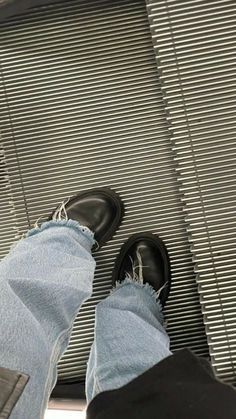 a person wearing black shoes and jeans standing in front of a window with blinds on it