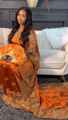 a woman in an orange and gold dress sitting on a couch holding a fur ball