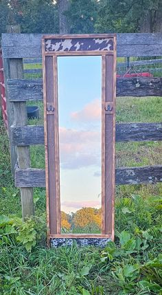 a mirror sitting in the grass next to a wooden fence with a sign on it