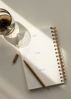 a glass of wine next to a notepad and pencil on a white table top