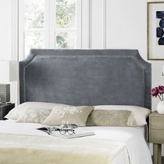 a bedroom with a gray upholstered headboard and eyeglasses on the bed