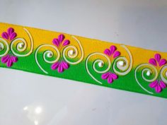 a yellow and green decorative ribbon with pink flowers on it's side, sitting on a white surface