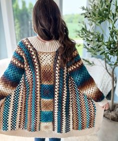 a woman standing in front of a window wearing a crocheted sweater