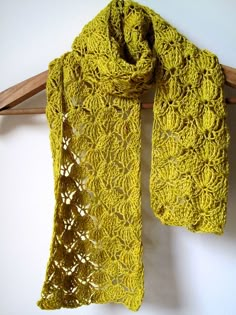 a yellow crocheted scarf hanging on a wooden hanger next to a white wall