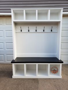 a white and black bench with two coats on it's back wall next to garage doors