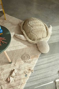 a turtle toy sitting on top of a rug next to a table with crayons