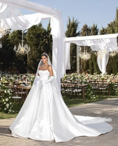 a woman in a white wedding dress standing under an arch with flowers and chandeliers