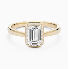 an emerald - cut diamond engagement ring in yellow gold with diamonds on the band and shoulders