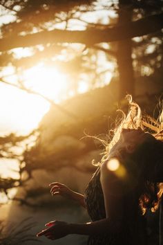 a woman with her hair blowing in the wind near some trees and sunbeams