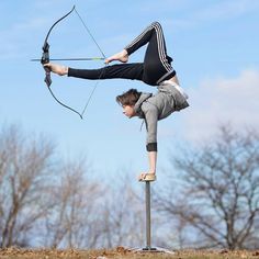 a woman standing on one leg while holding an arrow and aiming it at the ground