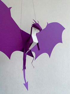 an origami dragon hanging from a string on the wall with purple and white paper