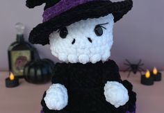 a crocheted teddy bear wearing a witches hat and holding a black candle holder