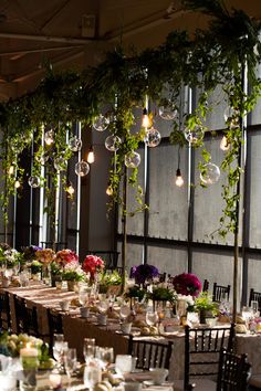 the tables are set up for an event with hanging lights and flowers in vases