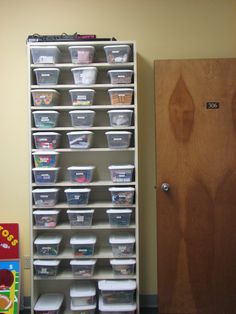 a shelf filled with lots of plastic containers next to a wooden door in a room