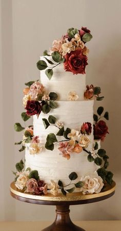 a three tiered white cake with flowers on the top and bottom, sitting on a wooden stand