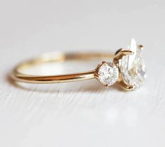 an engagement ring with two diamonds on it, sitting on top of a white surface