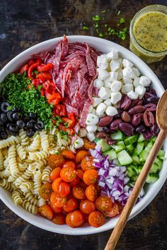 a bowl filled with pasta, meat and vegetables next to a glass of olive dressing